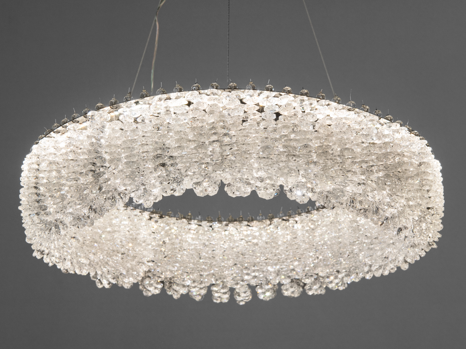 Кругла люстра з кришталевими підвісками, що створює ефект сяйва. Підвісна конструкція підходить для вітальні.