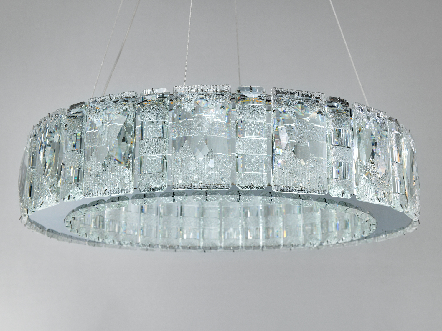 Люстра з прозорими кришталевими елементами, підвішена на тонких тросах, забезпечує рівномірне освітлення кімнати.