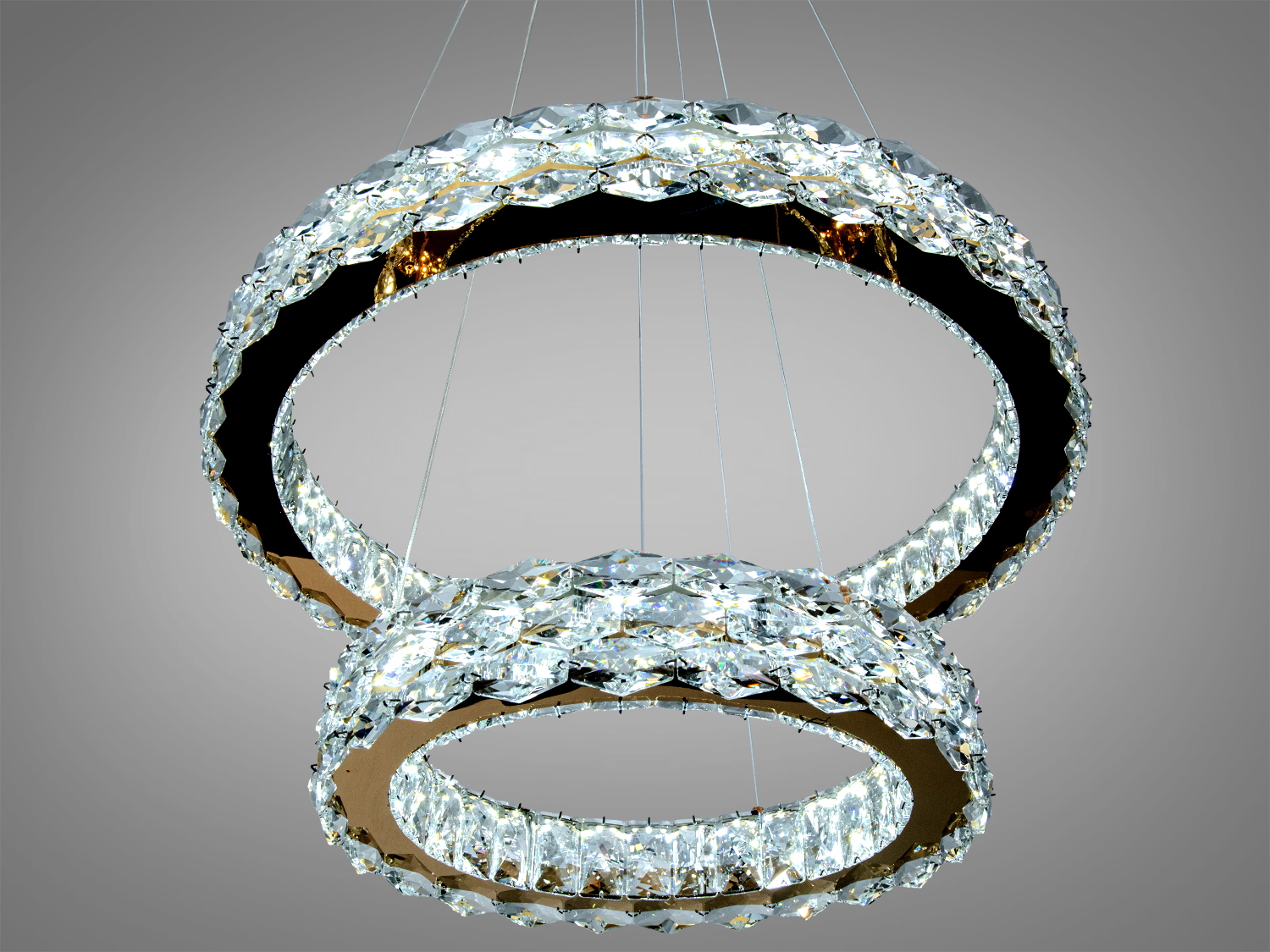 Люстра з двома блискучими кільцями з кристалів, підвішена близько до стелі, створює ефектний світловий акцент.