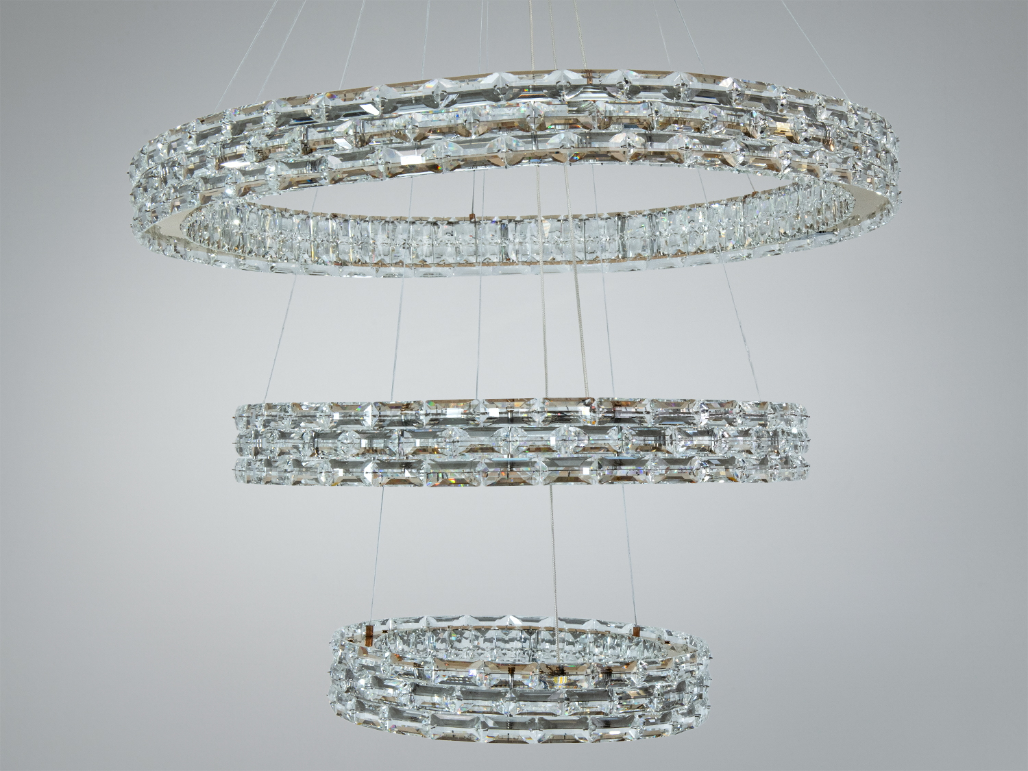 Люстра з трьома кристалічними кільцями, підвішена на тонких тросах, ідеальна для сучасного інтер′єру.