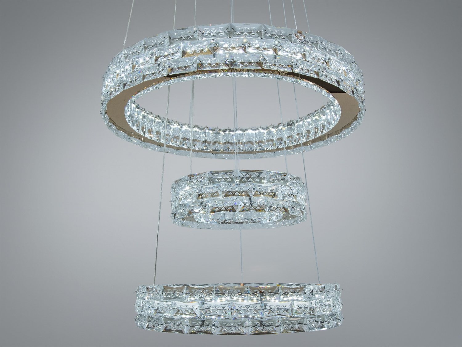 Кристалічна люстра з трьома кільцями, підвішена на тонких тросах. Ідеальна для освітлення просторих приміщень, створює ефект розсіяного світла.