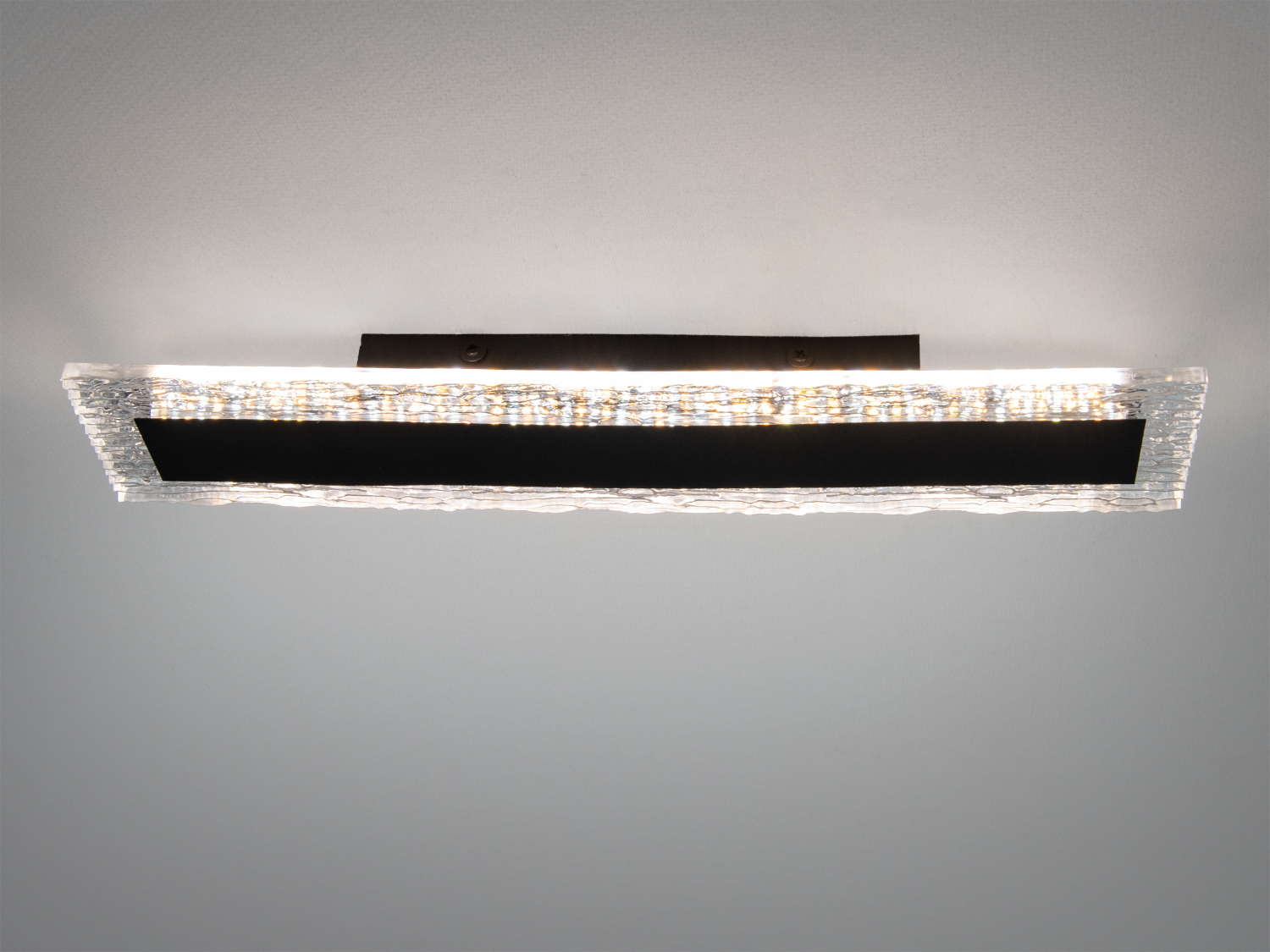 Світильник з монтажем на стелю, виконаний з текстурованого скла та чорного елемента. Забезпечує рівномірне освітлення приміщення.