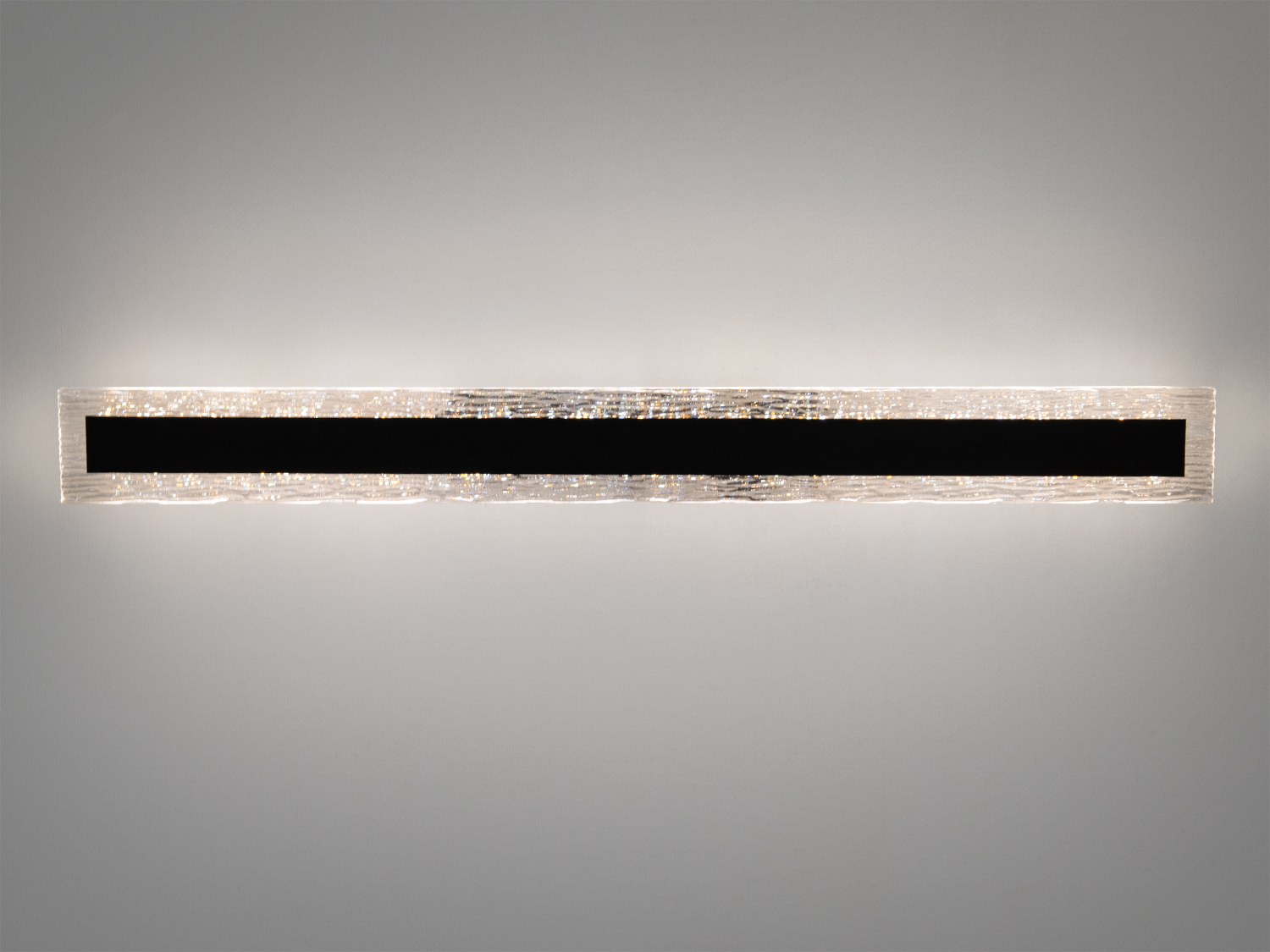 Лінійний світильник з текстурованого скла з чорною центральною смугою, що забезпечує рівномірне освітлення. Підходить для офісів.