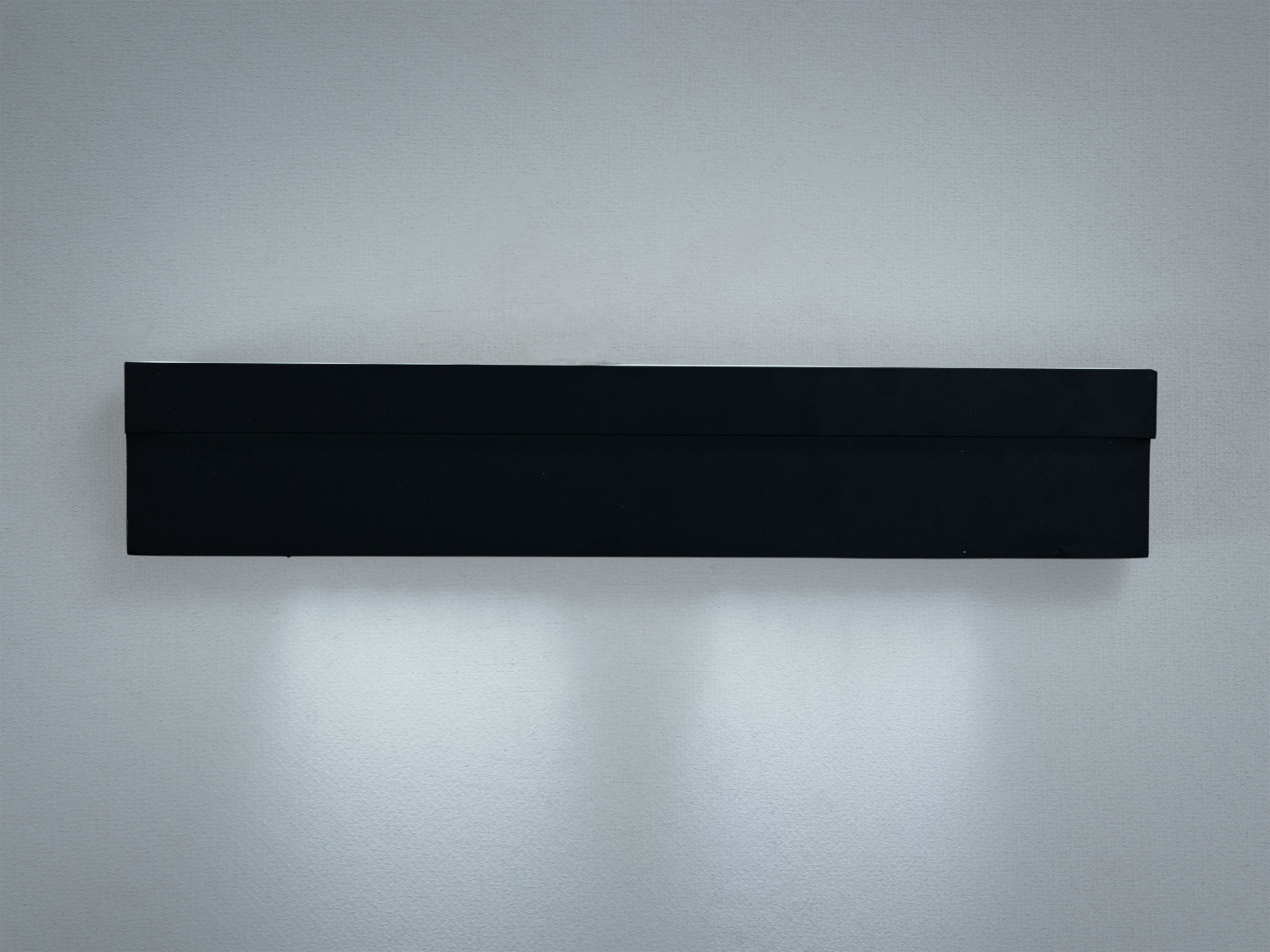 Прямокутний настінний світильник з чорного металу, розташований горизонтально. Підходить для освітлення віталень або коридорів.