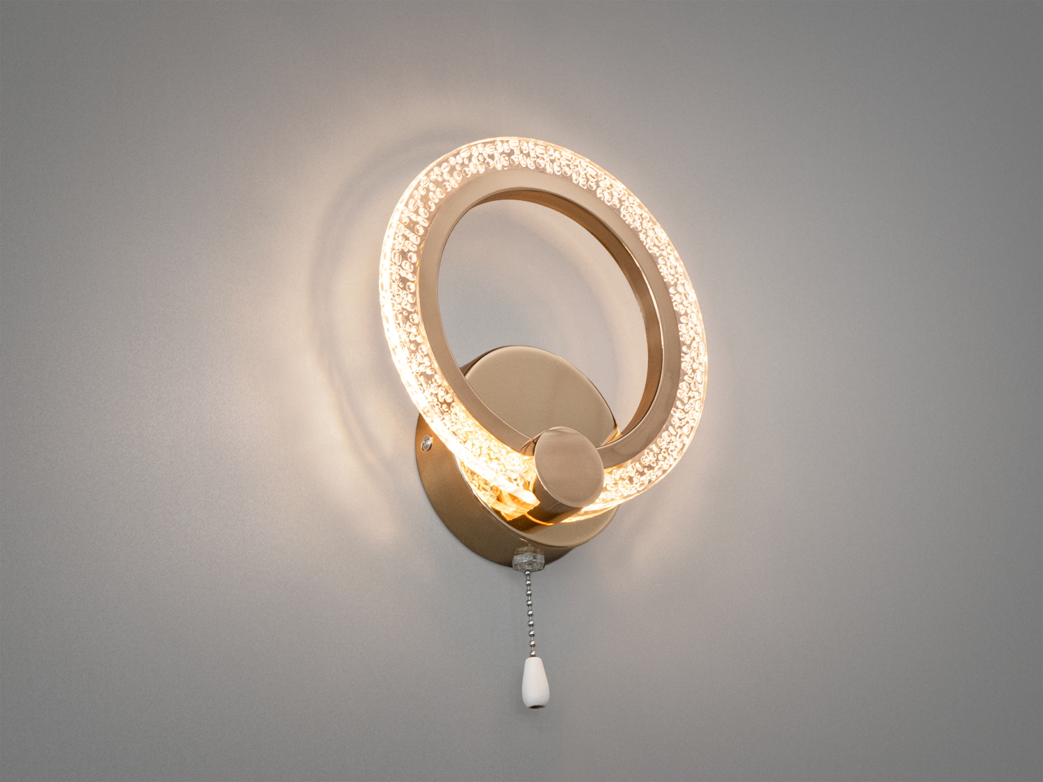 Настінний світильник з теплим жовтим світлом, кільцева форма з прозорими деталями. Оснащений ланцюжком для легкого увімкнення.