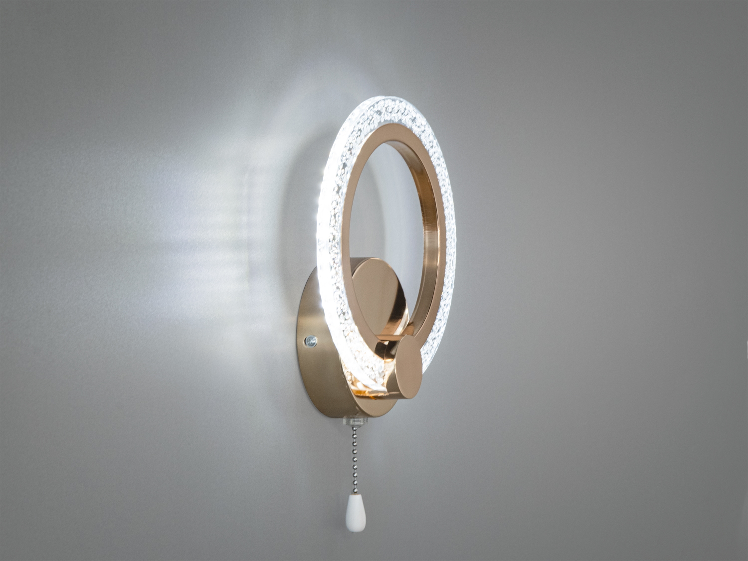 Сучасний настінний світильник з кільцевою конструкцією, що випромінює яскраве біле світло. Має зручний ланцюжок для керування.