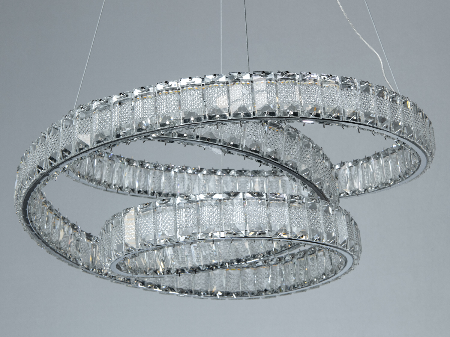 Люстра з трьома кришталевими кільцями, встановлена на металевій основі для рівномірного розподілу світла.