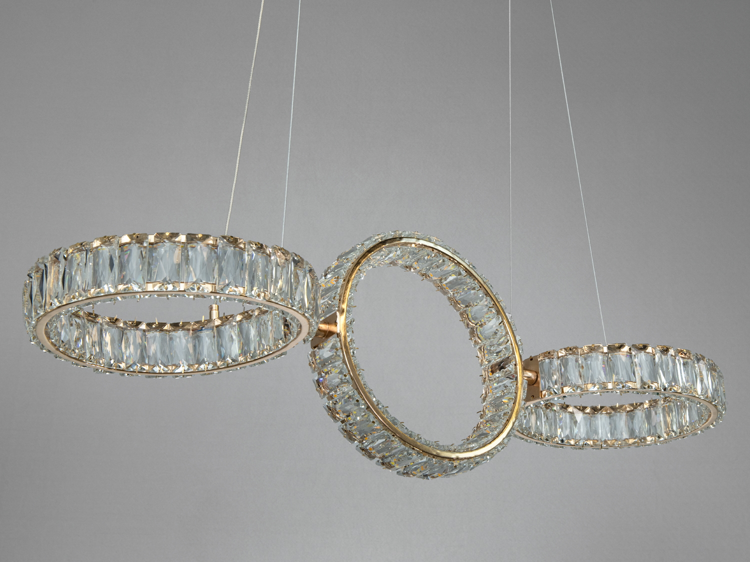 Три кільця люстри з прозорими кристалами, підвішені на тонких дротах, створюють елегантний вигляд.