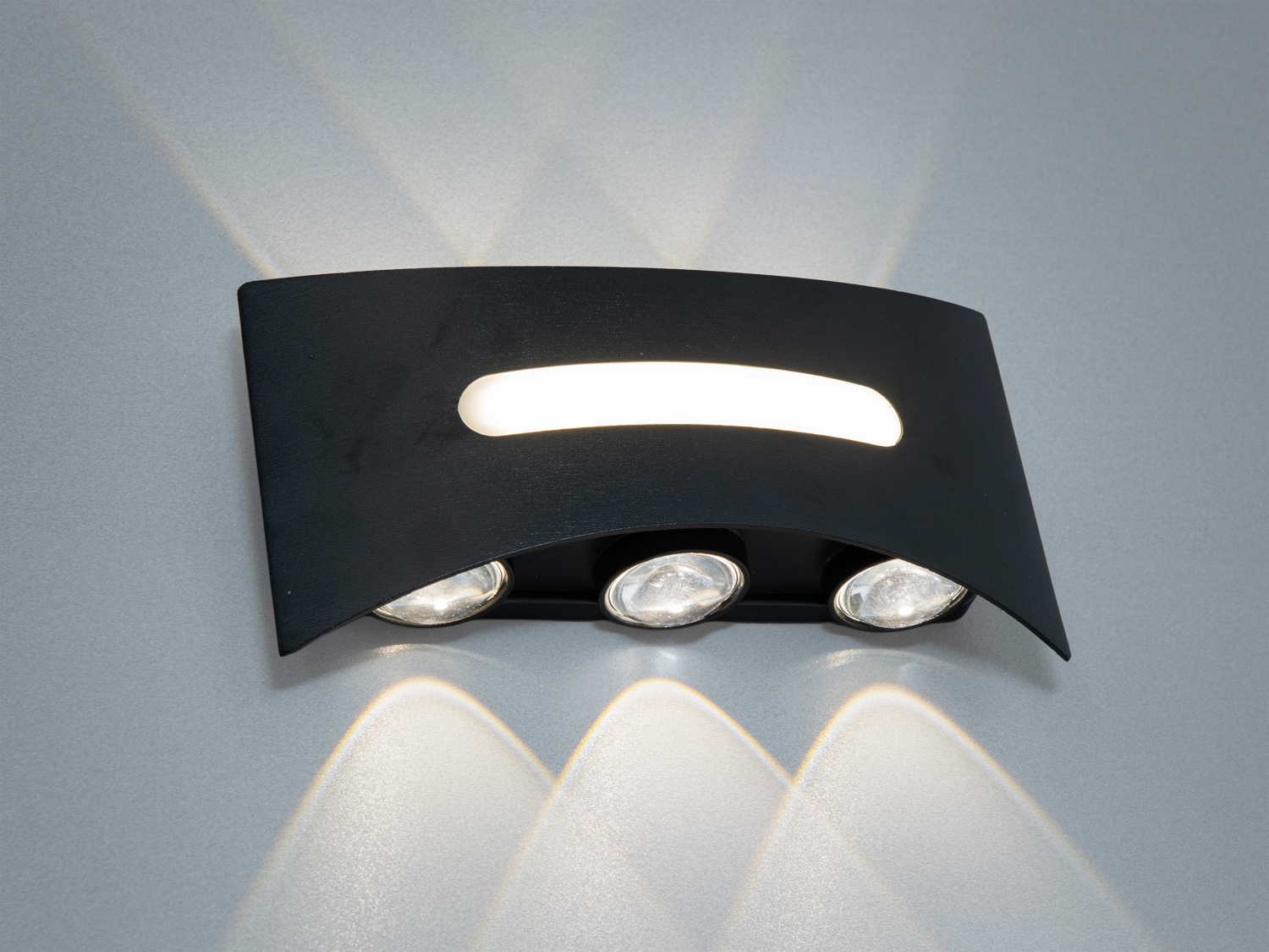 Настінний світильник з трьома точковими лампами під чорною вигнутою панеллю. Створює спрямоване освітлення, ідеально підходить для акцентного освітлення.