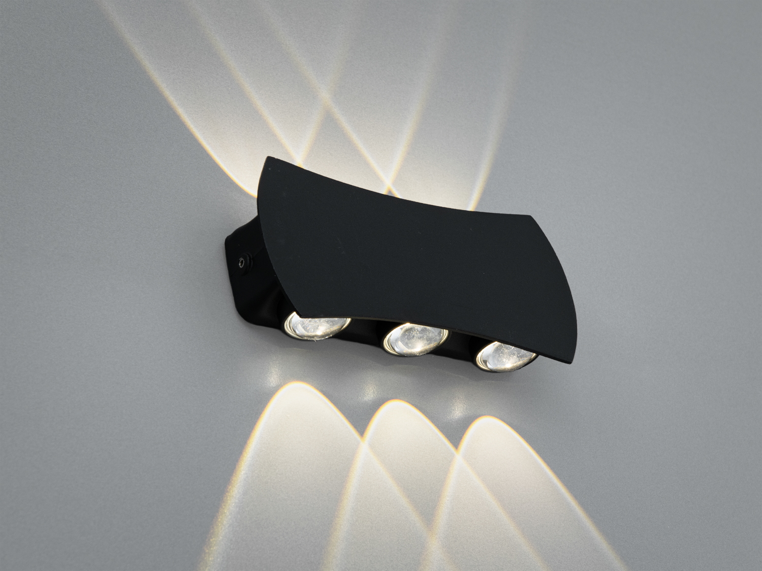 Чорний настінний світильник з трьома лампами, що випромінюють світло вгору і вниз, створюючи візерунки на стіні. Ідеальний для акцентного освітлення.