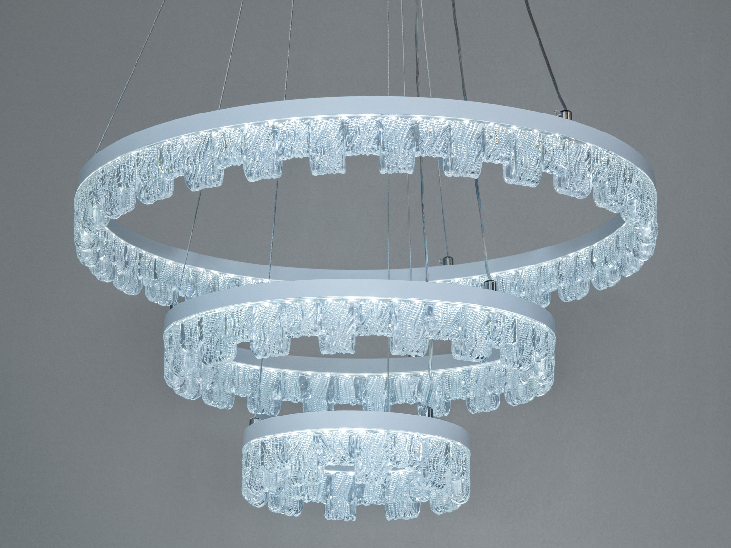 Три кільця підвісного світильника з LED-освітленням, підвішені на тонких тросах. Прозорі деталі надають йому елегантності, ідеальний для вітальні.