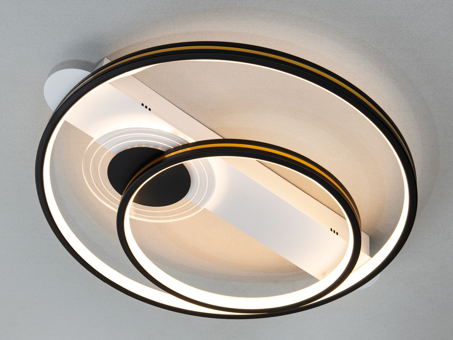Стельовий світильник з чорними кільцями, що випромінюють тепле світло. Підходить для затишних приміщень.