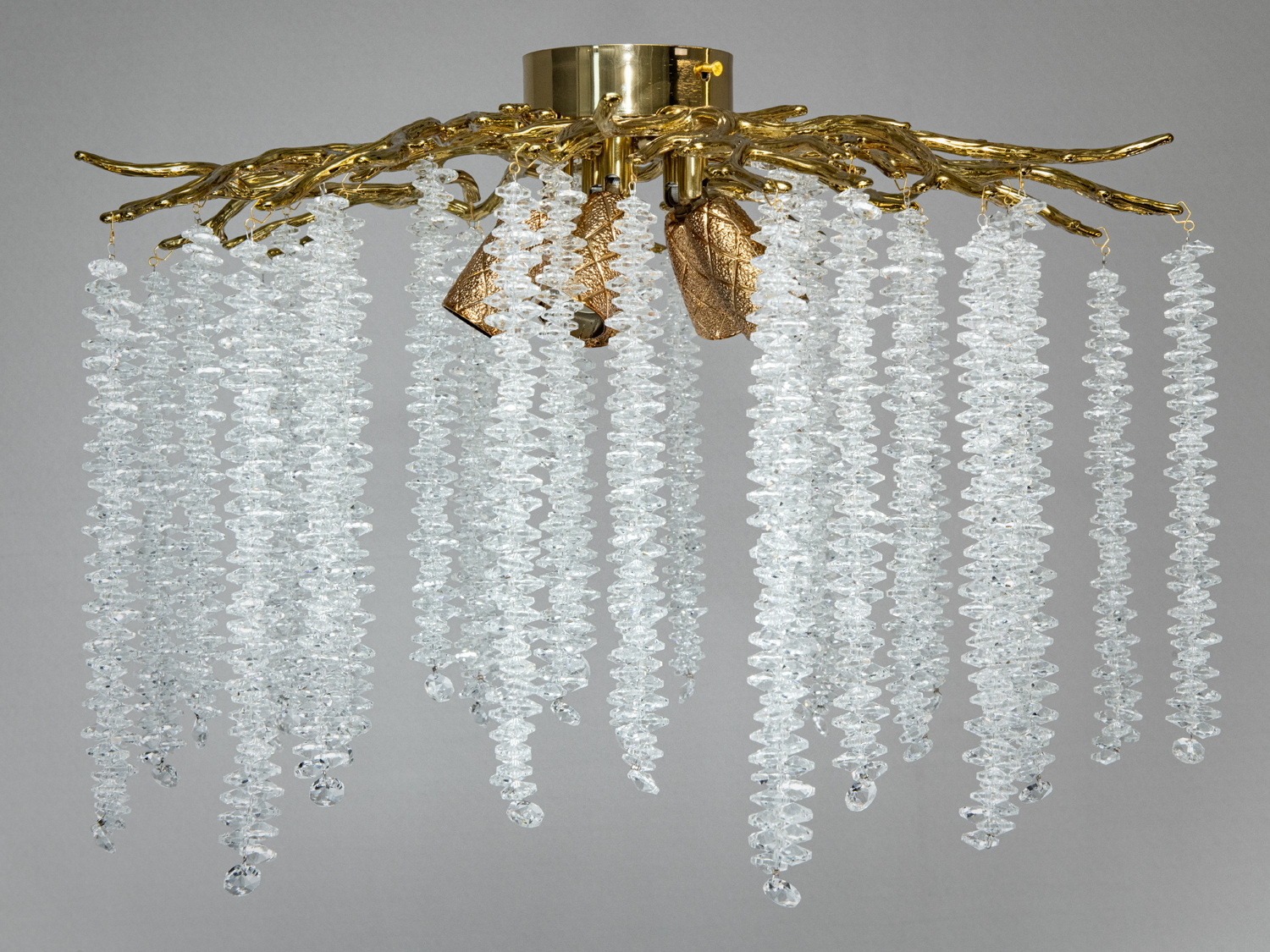 Підвісна люстра з кришталевими підвісками, що нагадують краплі води, на золотистій основі з гілками для сучасного інтер′єру.