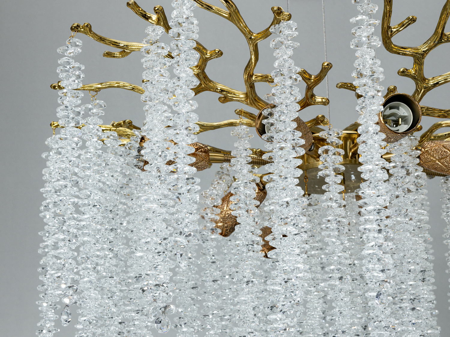 Деталь люстри з кришталевими підвісками, що нагадують лід, на золотистих гілках. Відмінний вибір для елегантного освітлення.