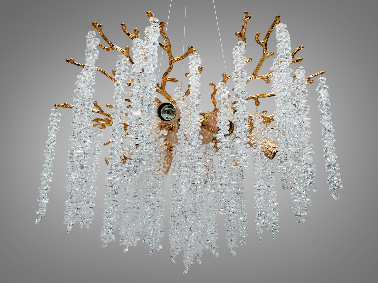 Люстра з кришталевими підвісками та золотистою основою, що нагадує гілки Гліцинії, підвішена на тонких тросах для сучасного інтер′єру.
