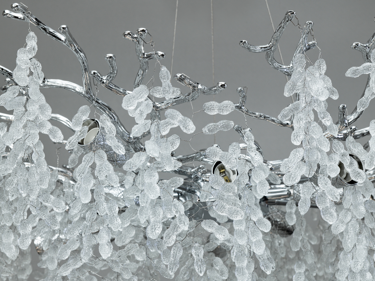Деталі люстри з блискучими металевими гілками та кришталевими підвісками, що нагадують сніжні шапки.