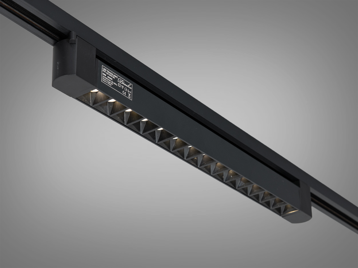 Трековий світильник чорного кольору з регульованим кутом нахилу, що дозволяє змінювати напрямок світла. Ідеальний для виставкових залів.