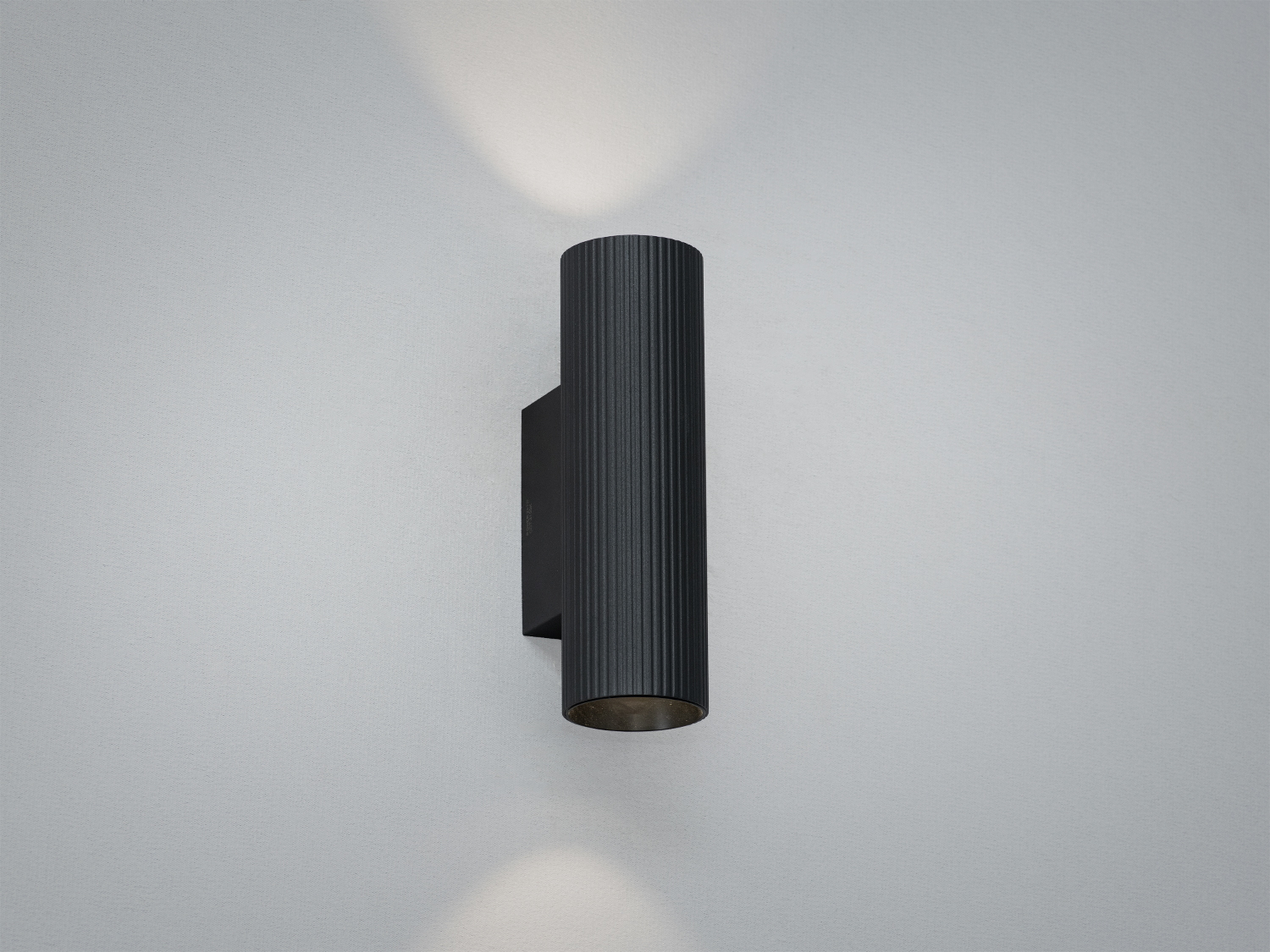 Настінний світильник циліндричної форми з чорного металу, випромінює світло вгору та вниз, підходить для сучасного інтер′єру.