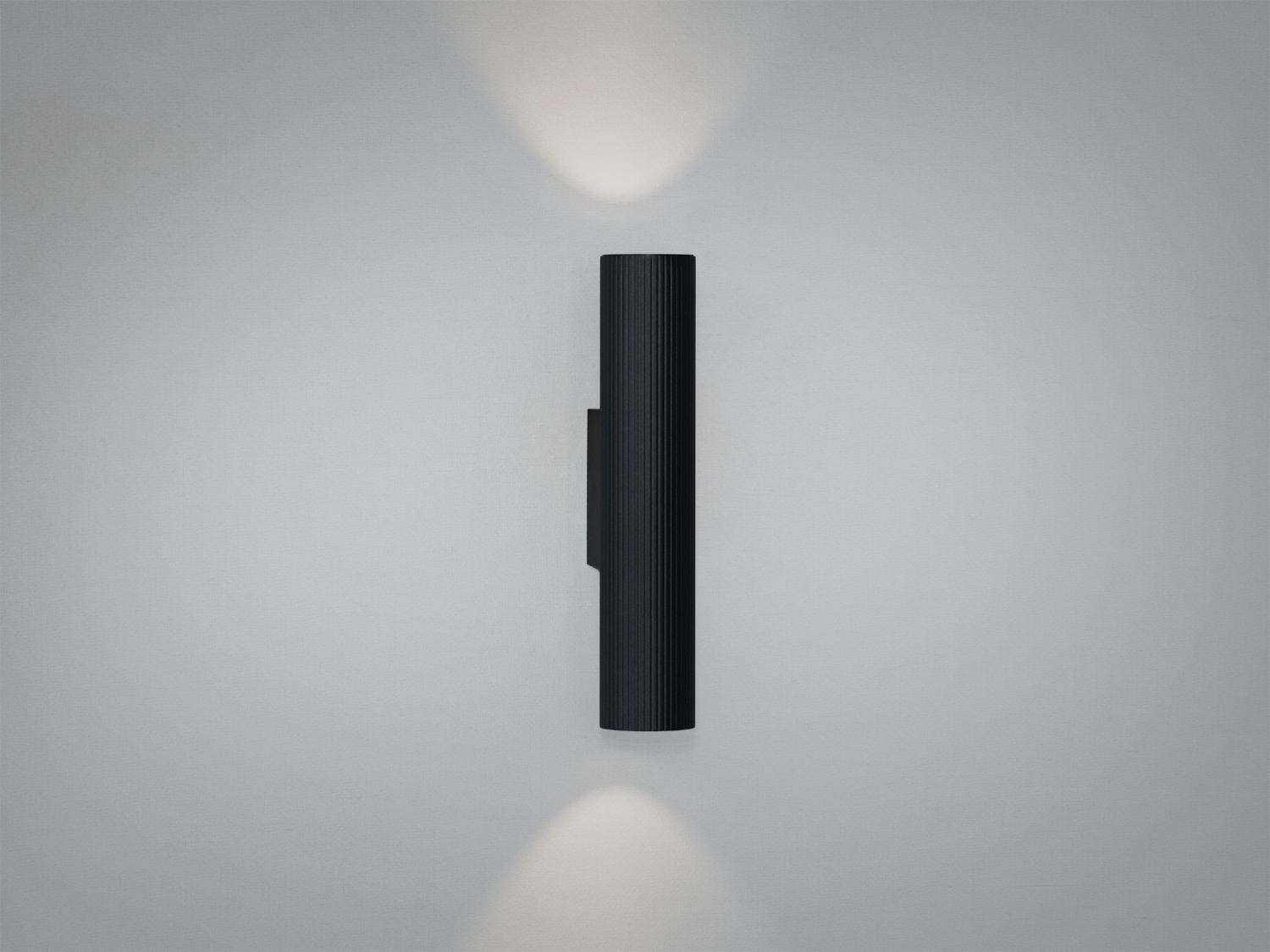 Настінний світильник циліндричної форми з чорного металу, випромінює світло вгору і вниз, підходить для сучасного інтер′єру.