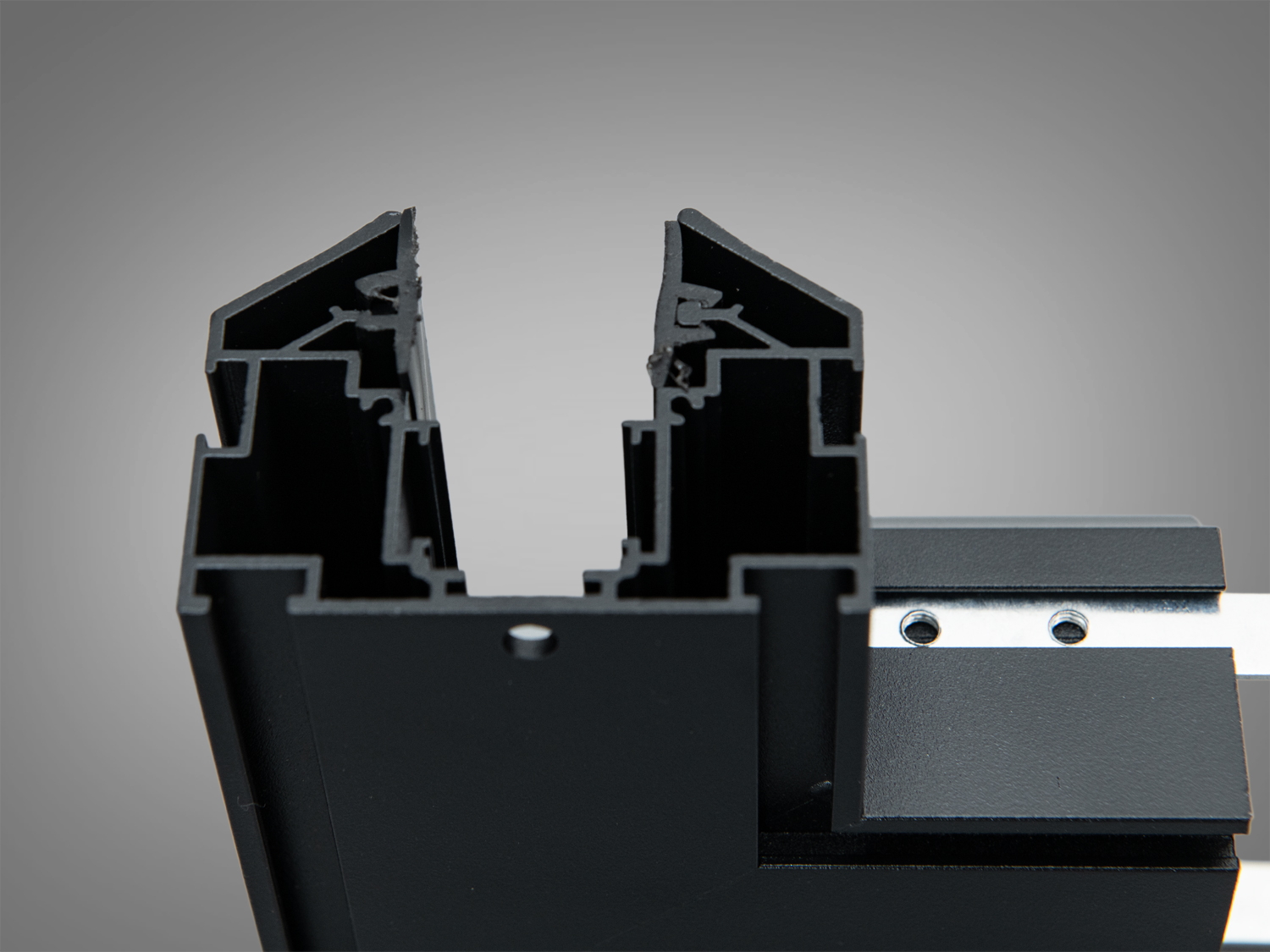 Профіль чорного кольору з відкритим зрізом, що демонструє внутрішню структуру. Призначений для використання в освітлювальних конструкціях.