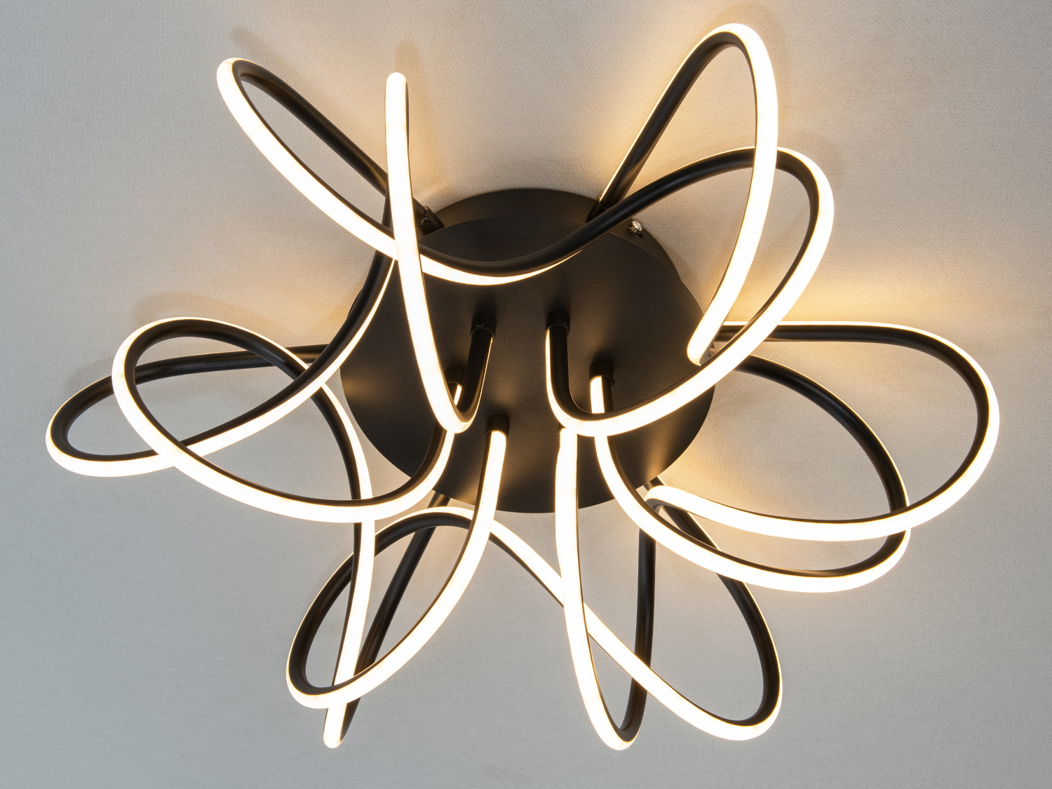 Дизайнерський світильник з чорними металевими елементами та теплими LED-смугами, що створюють динамічний візерунок для стелі.